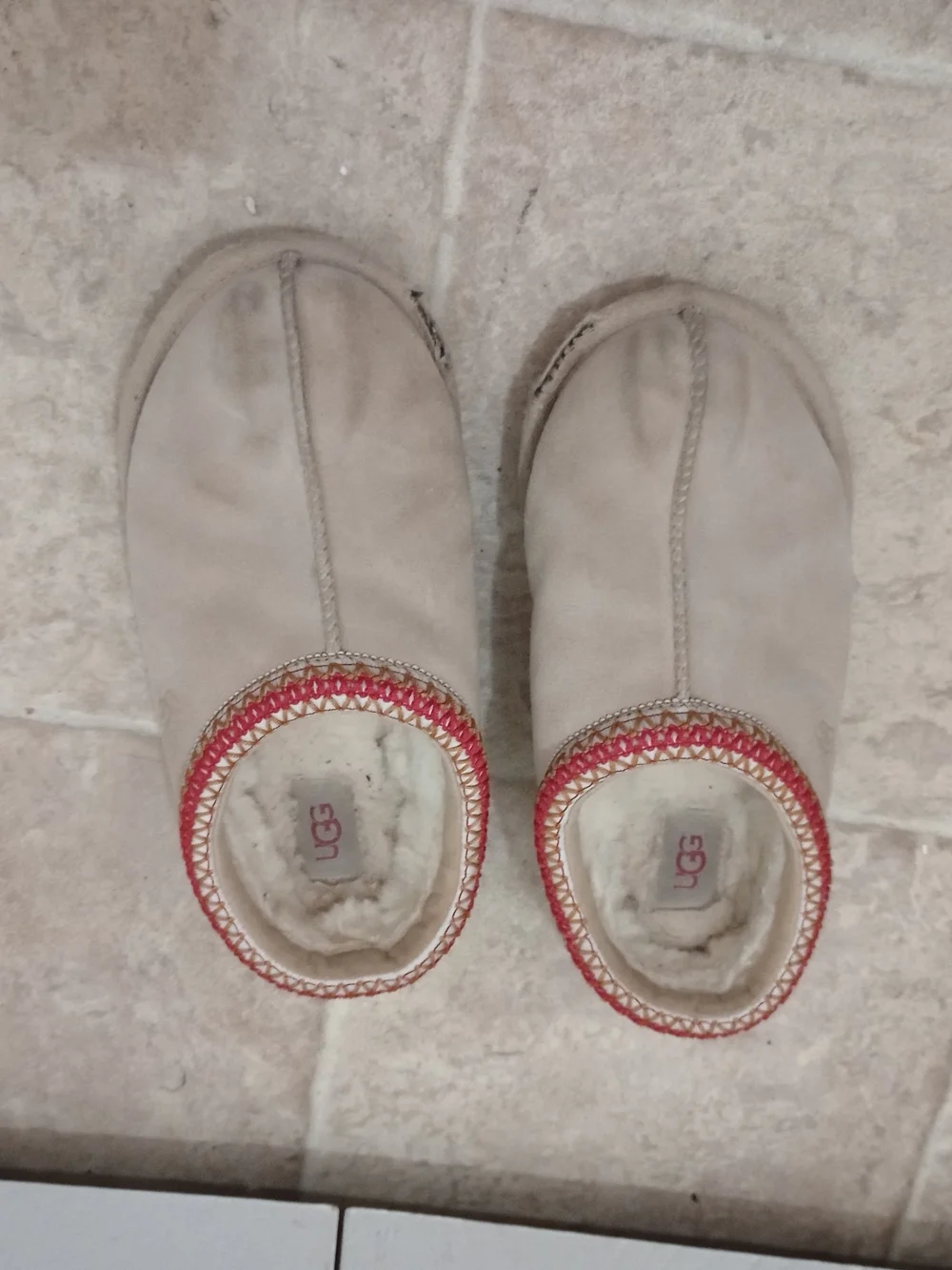 UGG Women's Tasman II slippers in a sand or beige color with red-patterned trim.